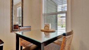 A dining area with a glass table, wicker chairs, a mirror, and a window with blinds. - Stones Throw Beachside Bungalow 1 ON THE Beach (Indian Rocks Beach)
