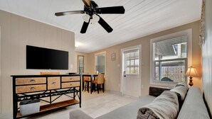 A living room with a flat-screen TV, a ceiling fan, a dining area with a table and chairs, and a sofa. - Stones Throw Beachside Bungalow 1 ON THE Beach (Indian Rocks Beach)