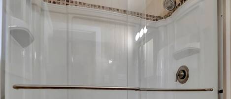 A glass-enclosed shower stall with a white tiled wall, a showerhead, and a control knob.