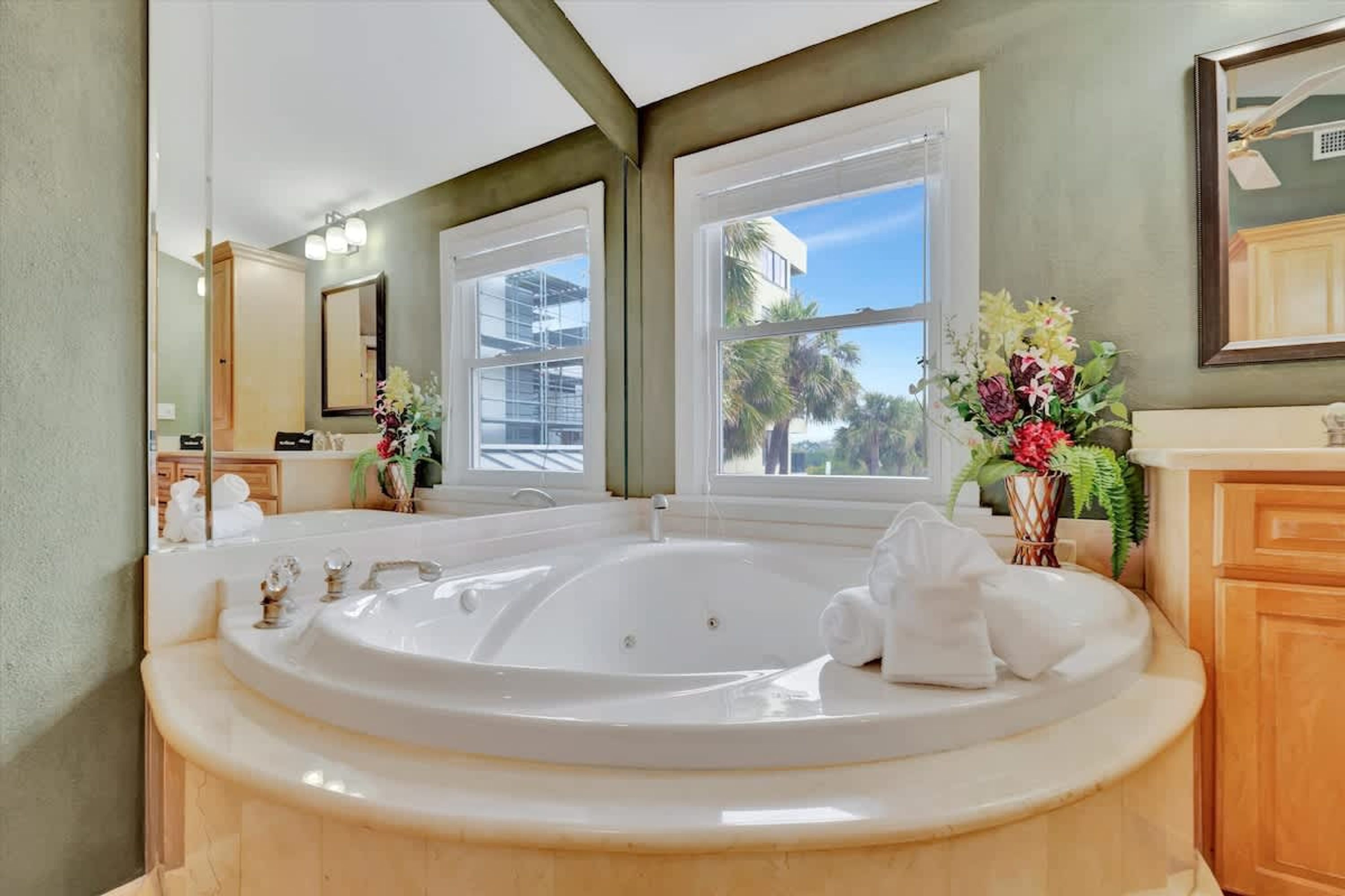 A bathroom with a large bathtub, a mirror, a window, and a sink.