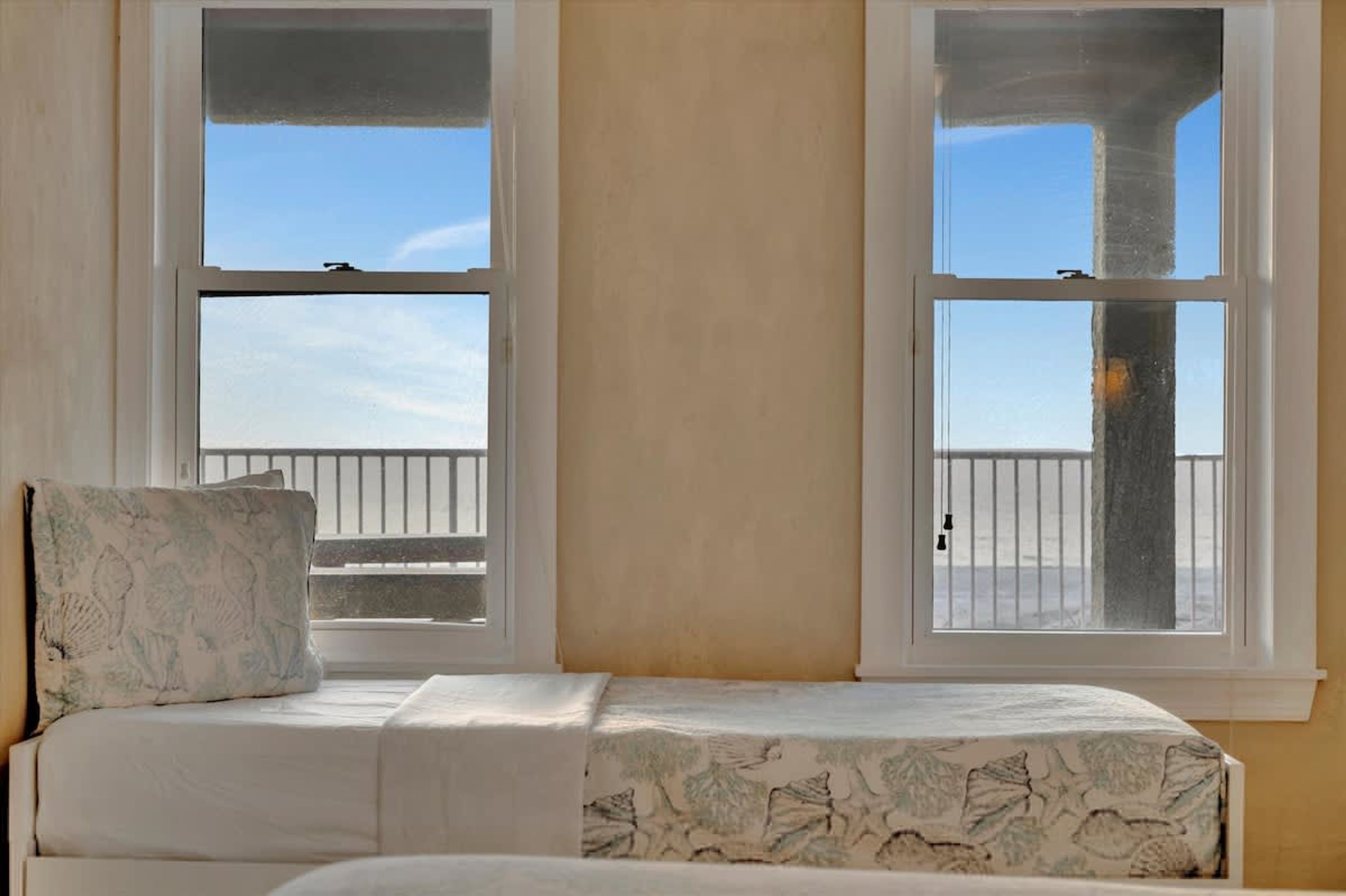 A bedroom with a bed, two windows, and a view of the beach.