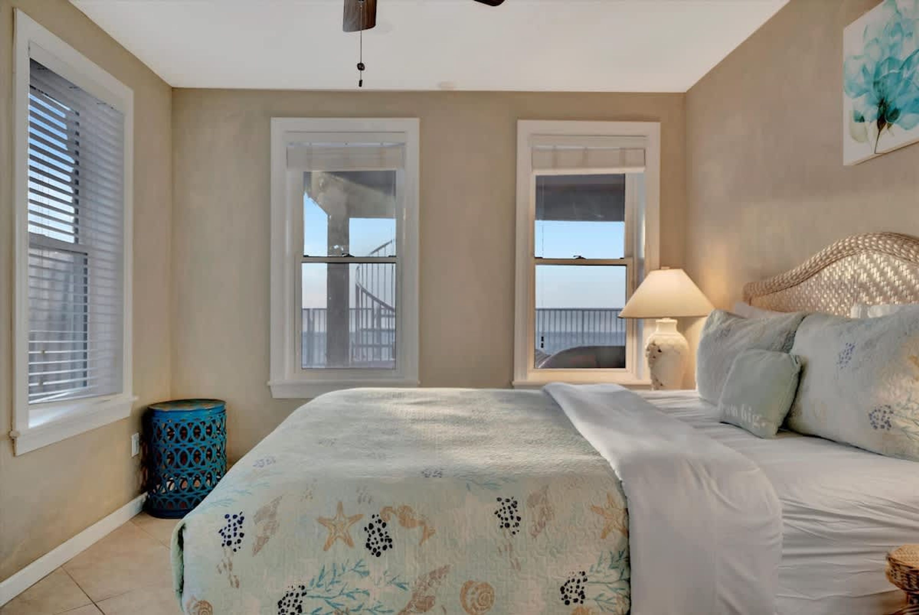 Un dormitorio con cama, mesita de noche, lámpara y vistas al exterior.