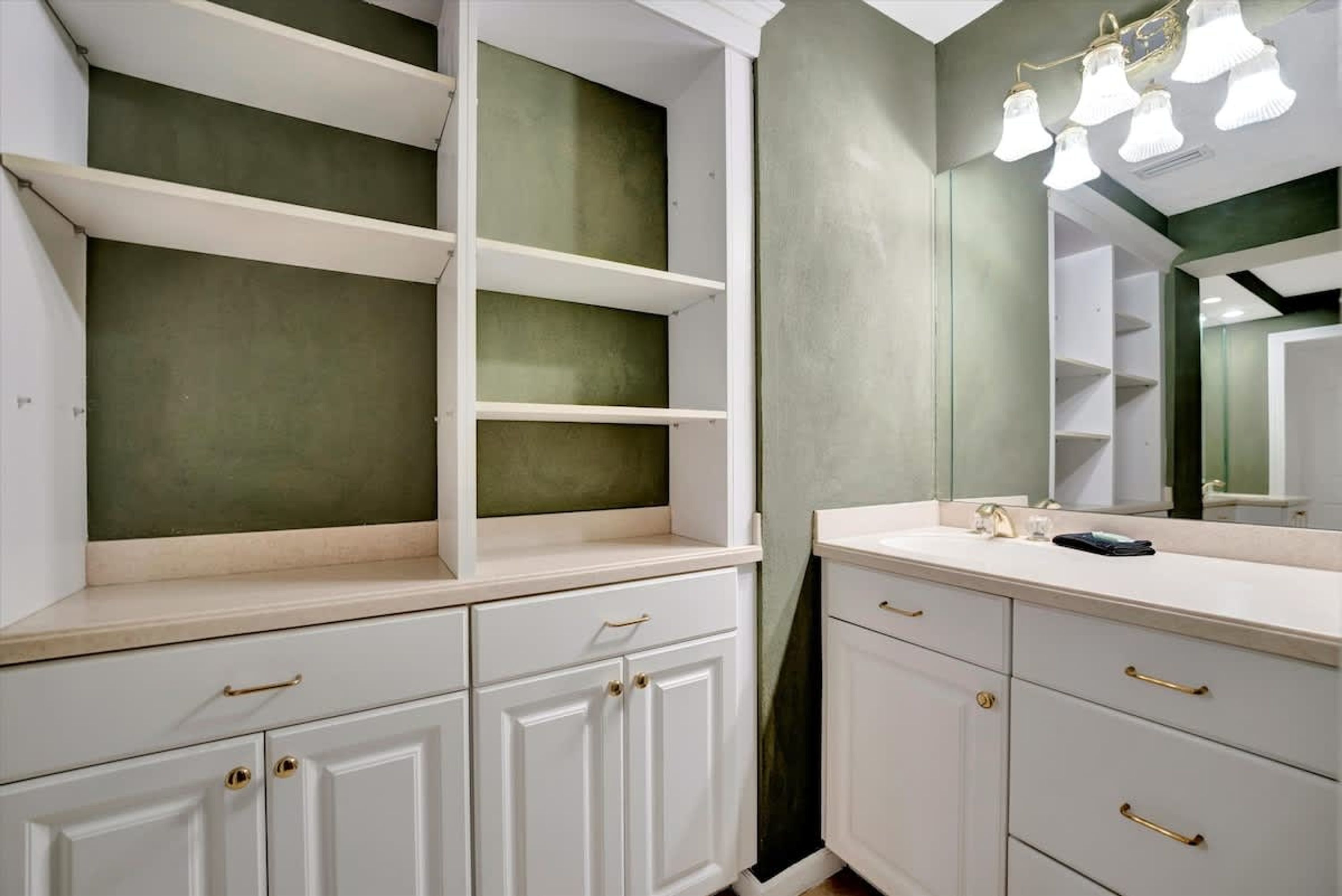 Un baño con muebles blancos, un espejo y una lámpara.