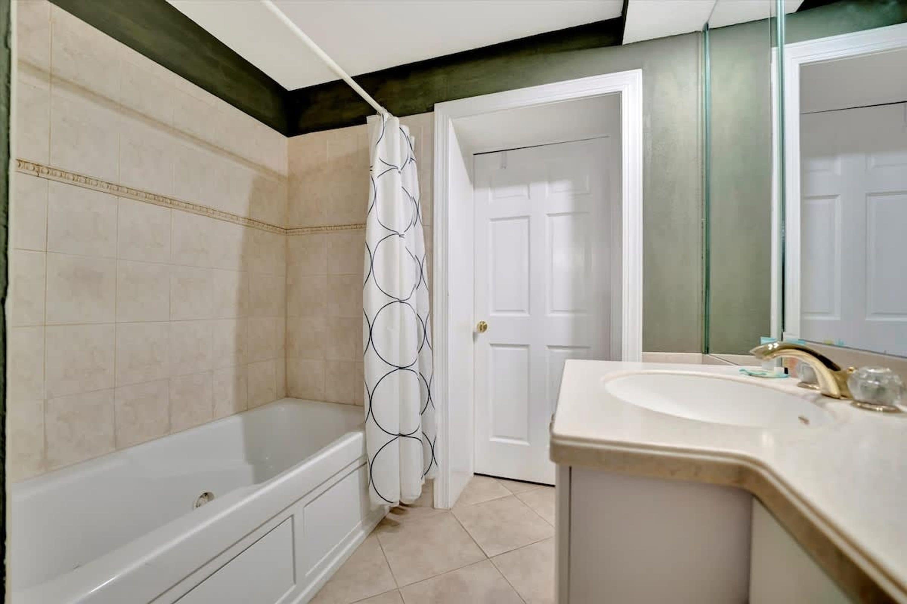 Un baño con bañera, cortina de ducha, lavabo y puerta.