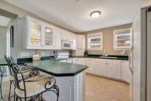A kitchen with white cabinets, a green countertop, and a built-in island with seating. - Stones Throw Beachfront Family Suite 3 Views (Indian Rocks Beach)