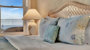 Een bed met een geweven hoofdbord, een lamp en uitzicht op de zee door een raam.