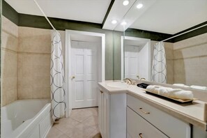 A modern bathroom with a bathtub, a shower with a patterned curtain, a large mirror, and a vanity with a towel rack. - Stones Throw Beachfront Family Suite 3 Views (Indian Rocks Beach)