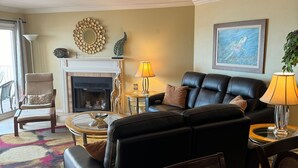 Una sala de estar con chimenea, un sofá de cuero negro, una mesa de centro redonda y una mesa de comedor.