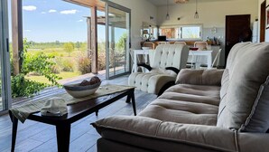 A modern living room with a large sliding glass door leading to a patio, a dining area with a kitchen in the background, and a sofa with a view. - La Colina by Carmelodays (Carmelo)