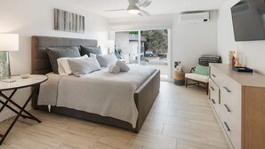 Un dormitorio moderno con una cama grande, ventilador de techo, televisor y vistas al exterior.
