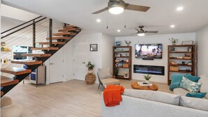 Una sala de estar moderna con una escalera, una chimenea y un televisor.