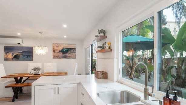 Una cocina moderna con armarios blancos, encimera de mármol y un ventanal con vistas a la vegetación.