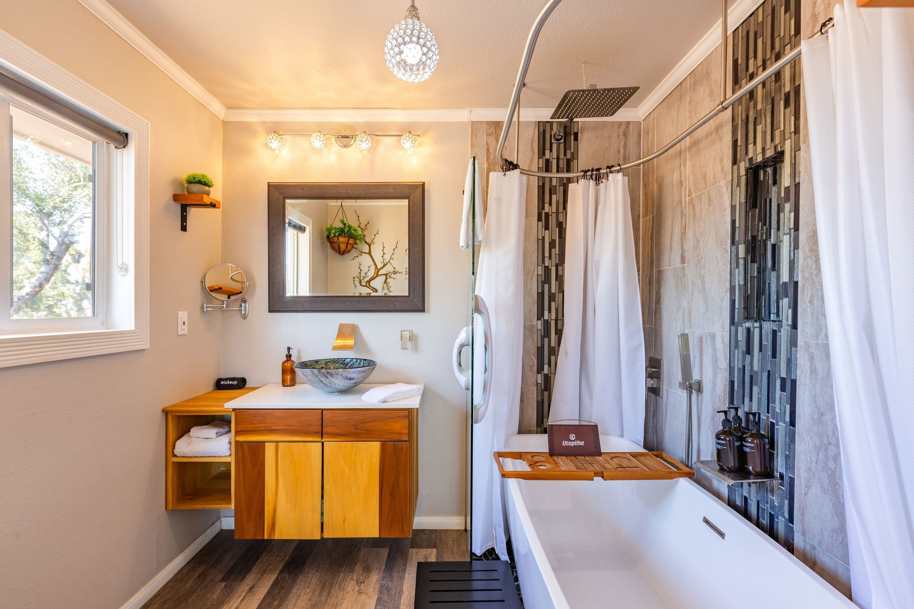 A modern bathroom with a wooden vanity, a large mirror, a hanging plant, and a shower with a glass door.