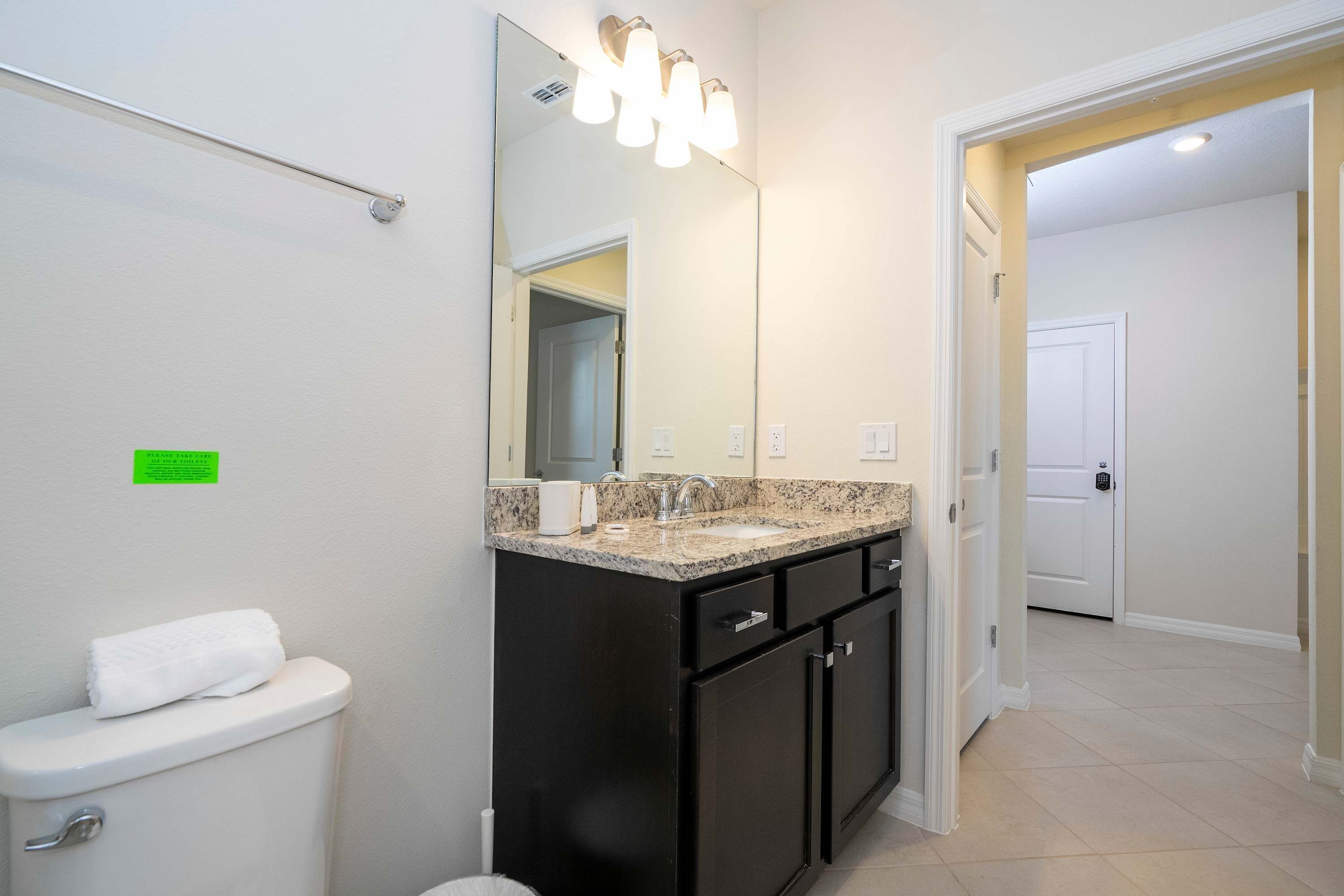 Une salle de bain comprenant des toilettes, un lavabo avec un plan de travail en granit, un miroir et un luminaire placé au-dessus du miroir.