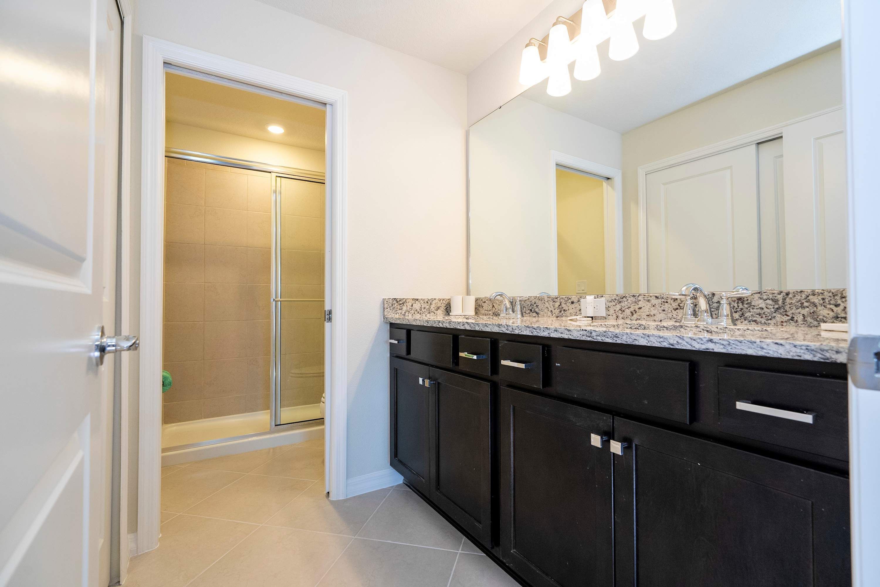 A bathroom with a shower, a sink with a mirror, and dark cabinets.