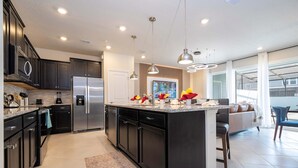 A modern kitchen with dark cabinetry, stainless steel appliances, and pendant lighting.