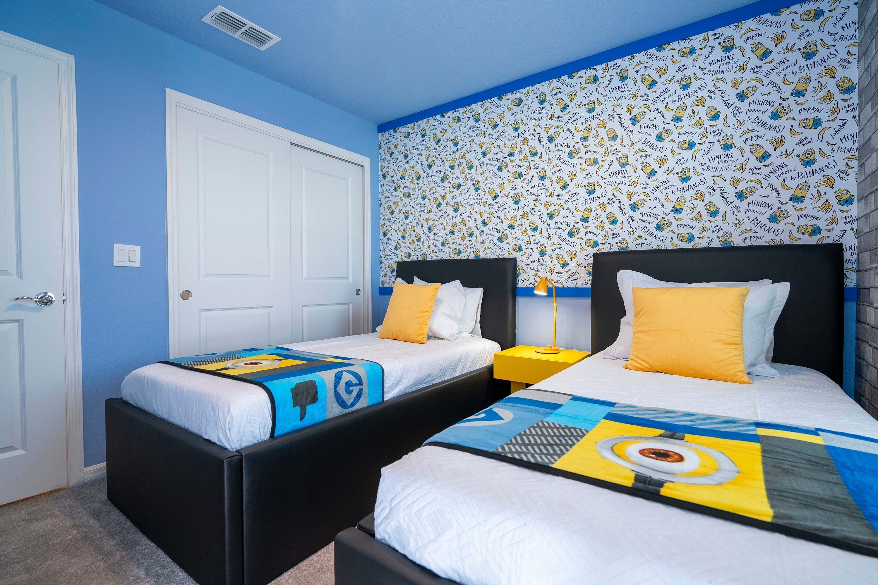 A room with two beds, a white door, and a wall with a Minions pattern.