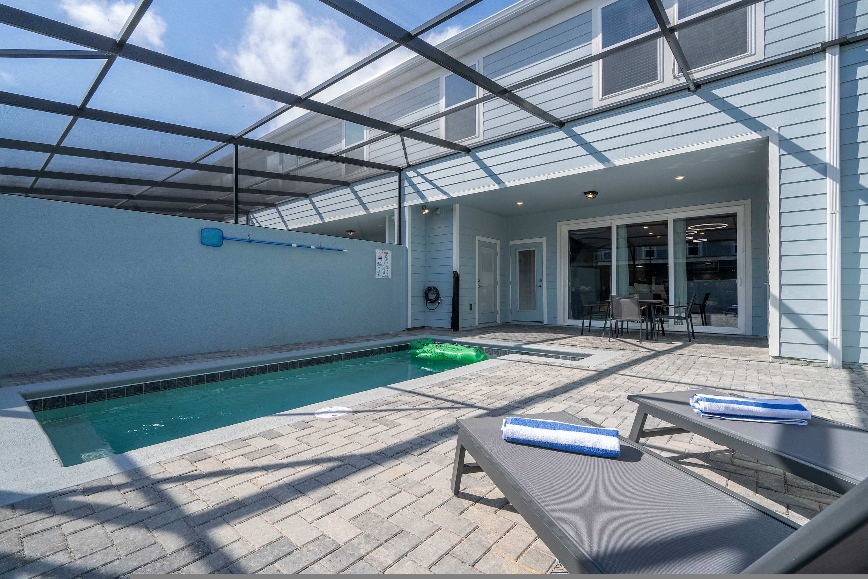 A pool area with a glass enclosure, lounge chairs, and a patio with outdoor furniture.