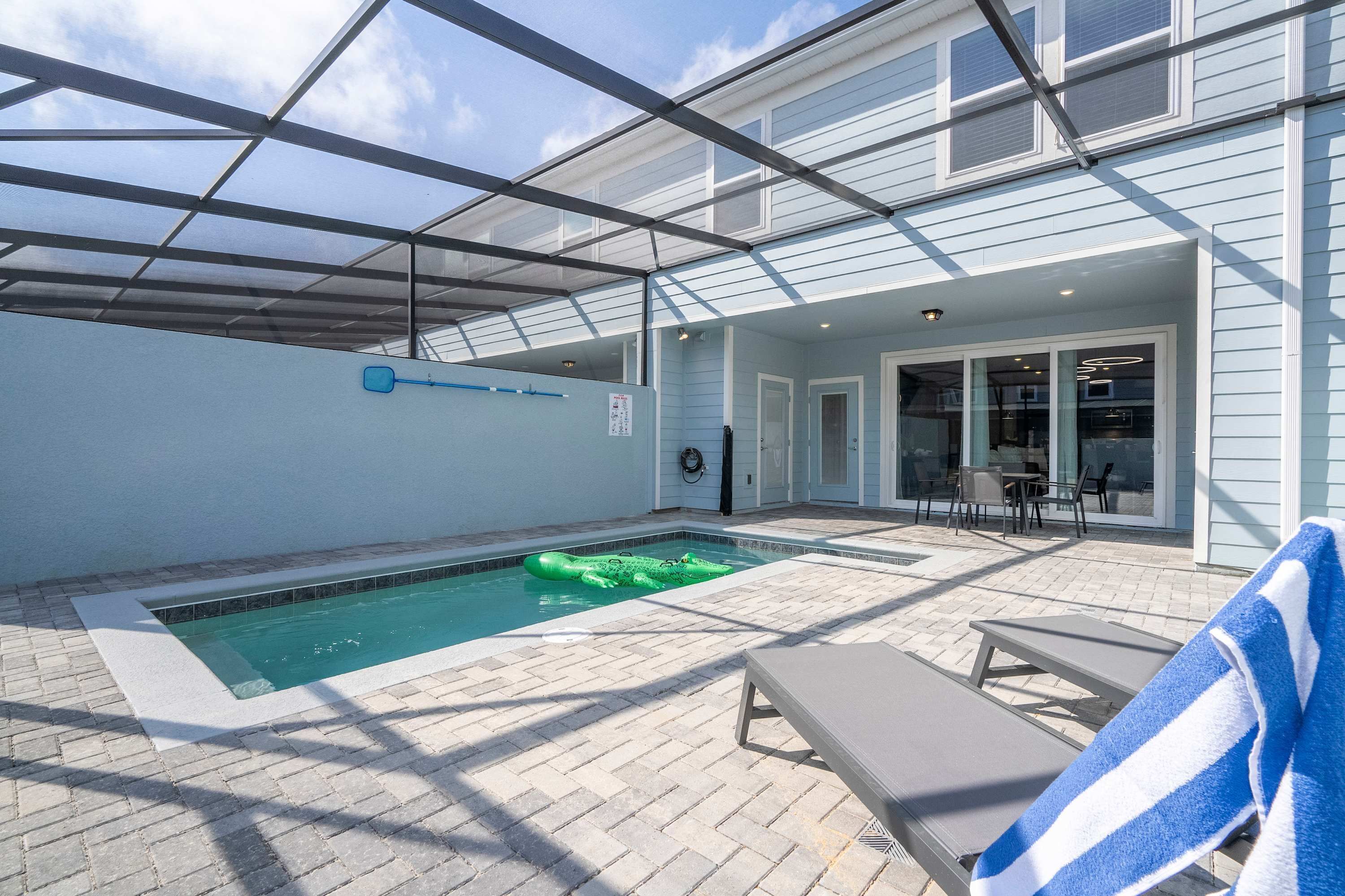 Une piscine extérieure dotée d’une structure en verre, de chaises longues et d’un espace patio avec une table et des chaises.