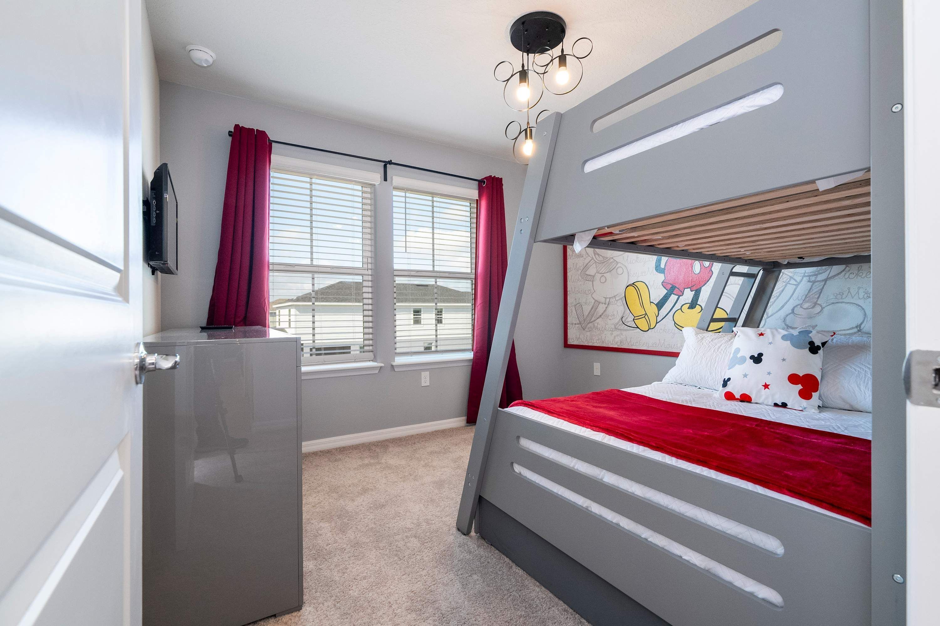 Quarto com beliche, uma escrivaninha pequena, janela com cortinas e luminária no teto.