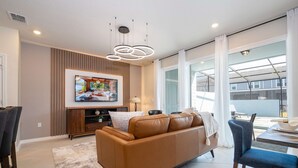 A modern living room with a brown leather sofa, a flat-screen TV mounted on a wooden cabinet, and a dining area with a table and chairs.