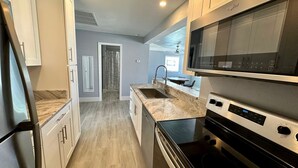 A modern kitchen with a microwave, oven, and stainless steel appliances. There is a window with a view of the outdoors. - Lil Lavender Whole House (Fort Myers Beach)