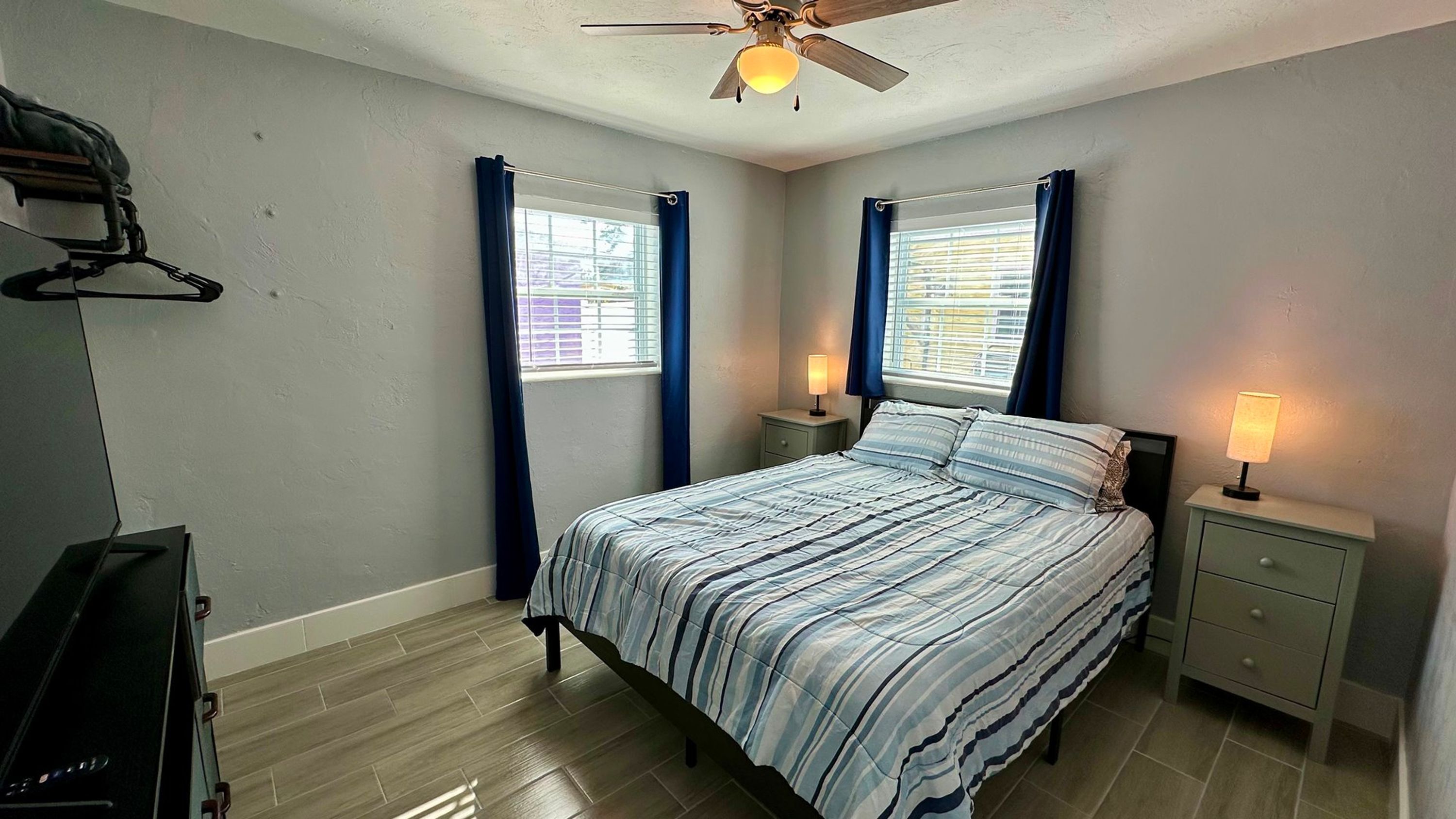 A bedroom with a bed, two bedside tables with lamps, a ceiling fan, and a window with curtains.