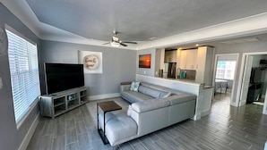 A modern living room with a grey sofa, a flat-screen TV, and a ceiling fan. - Lil Lavender Whole House (Fort Myers Beach)