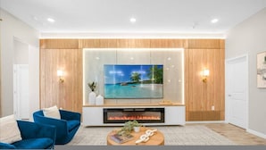 A modern living room with a flat-screen TV mounted on a wooden wall, a fireplace below, and a blue sofa. - Paradiso 12bd Pool Summerkitchen Gameroom Cinema (Orlando)
