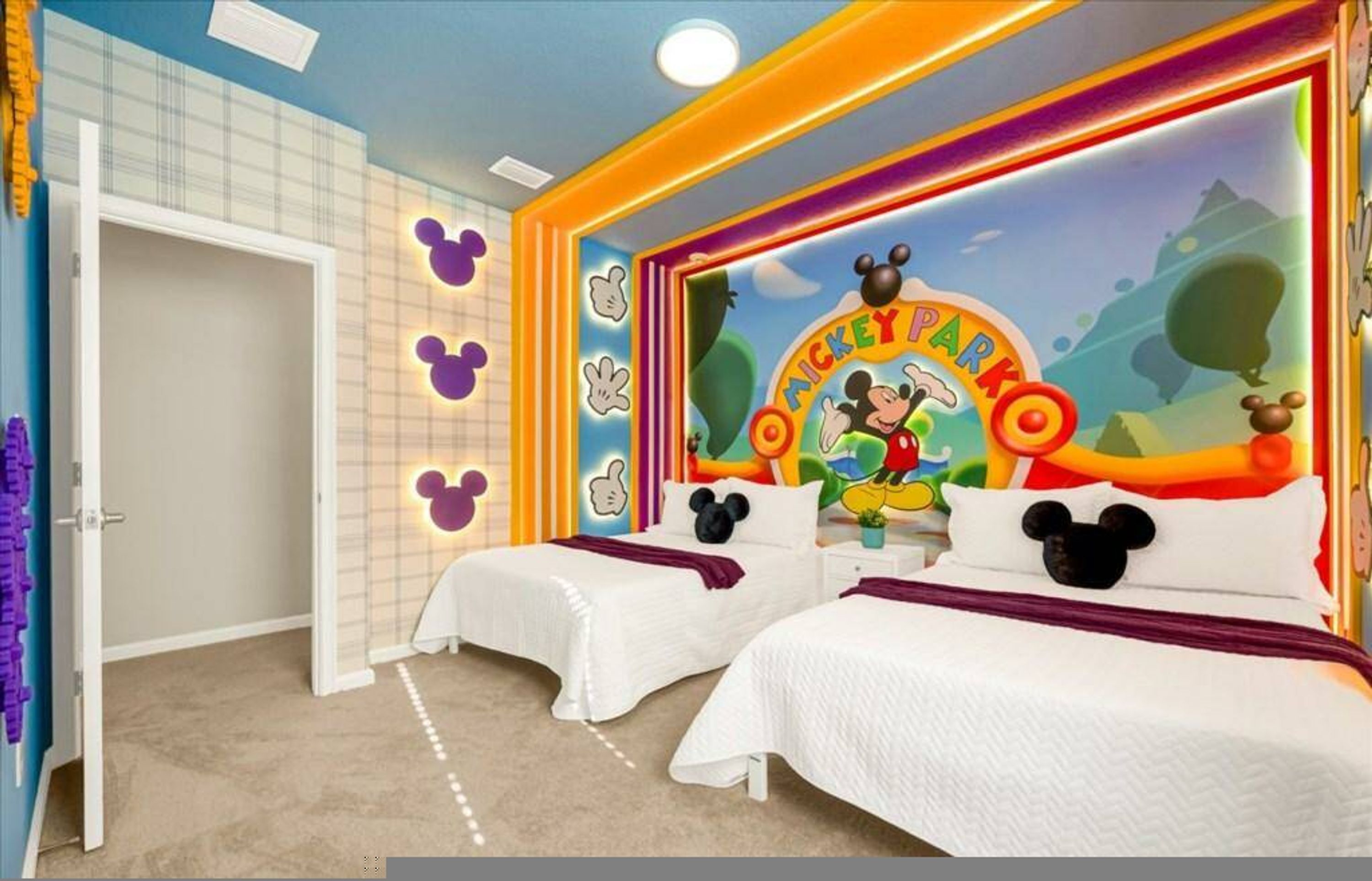 Une chambre d’enfant avec deux lits, une fresque représentant Mickey Mouse et une porte décorée de motifs violets.