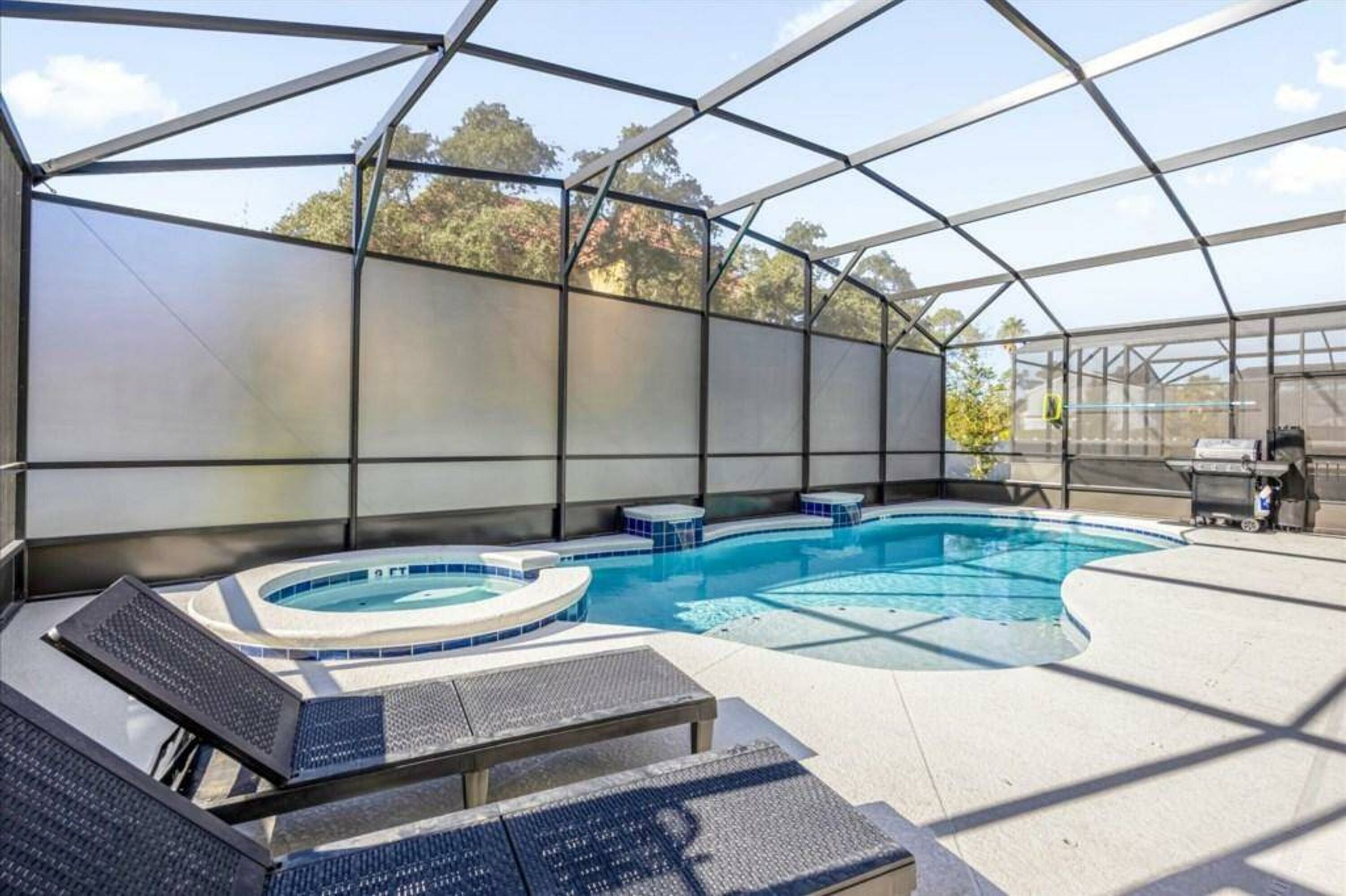 A covered outdoor swimming pool with lounge chairs, a hot tub, and a barbecue area.