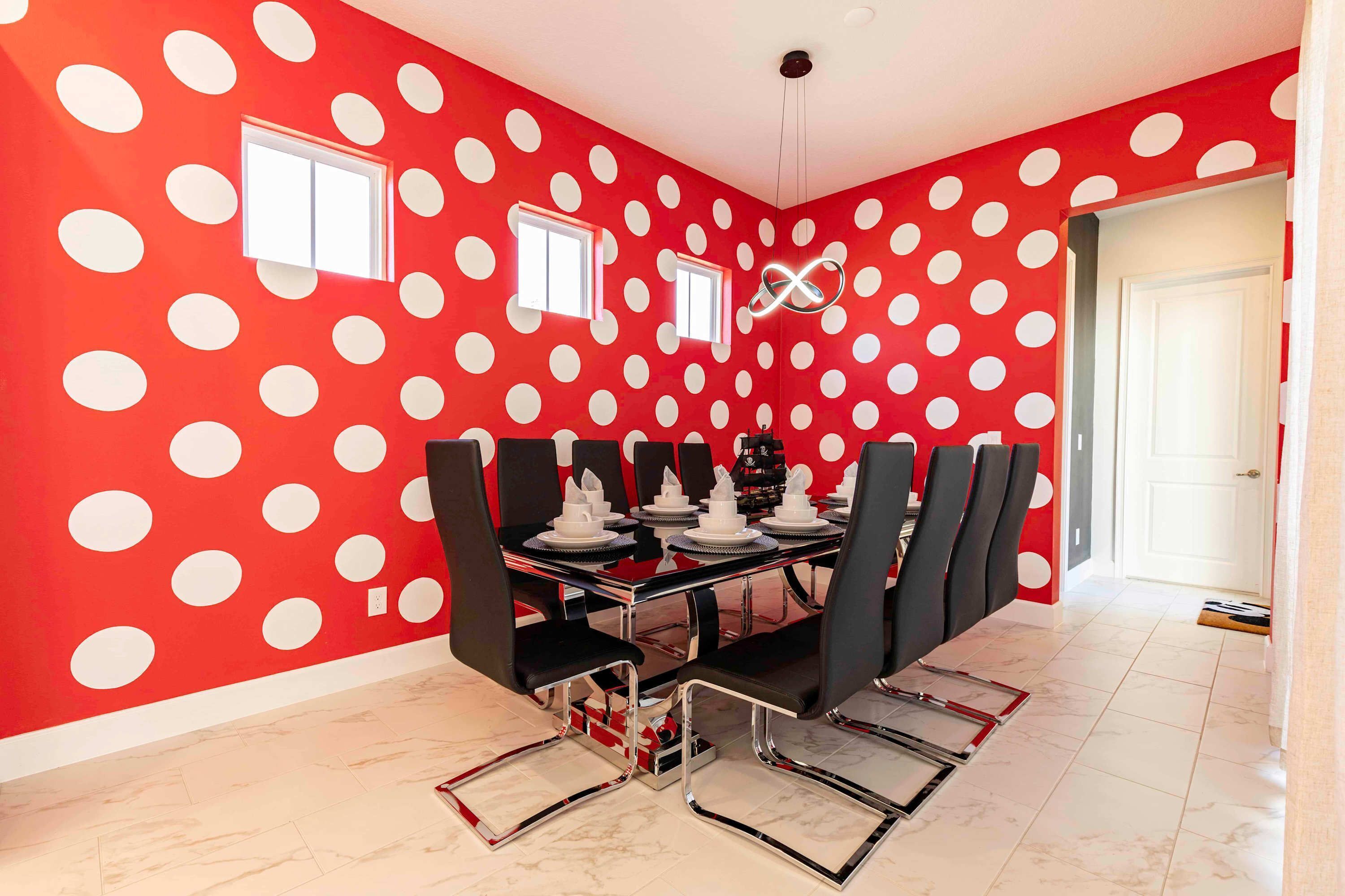 A dining area with a red polka dot wall, a black table with chairs, and a white door in the background.
