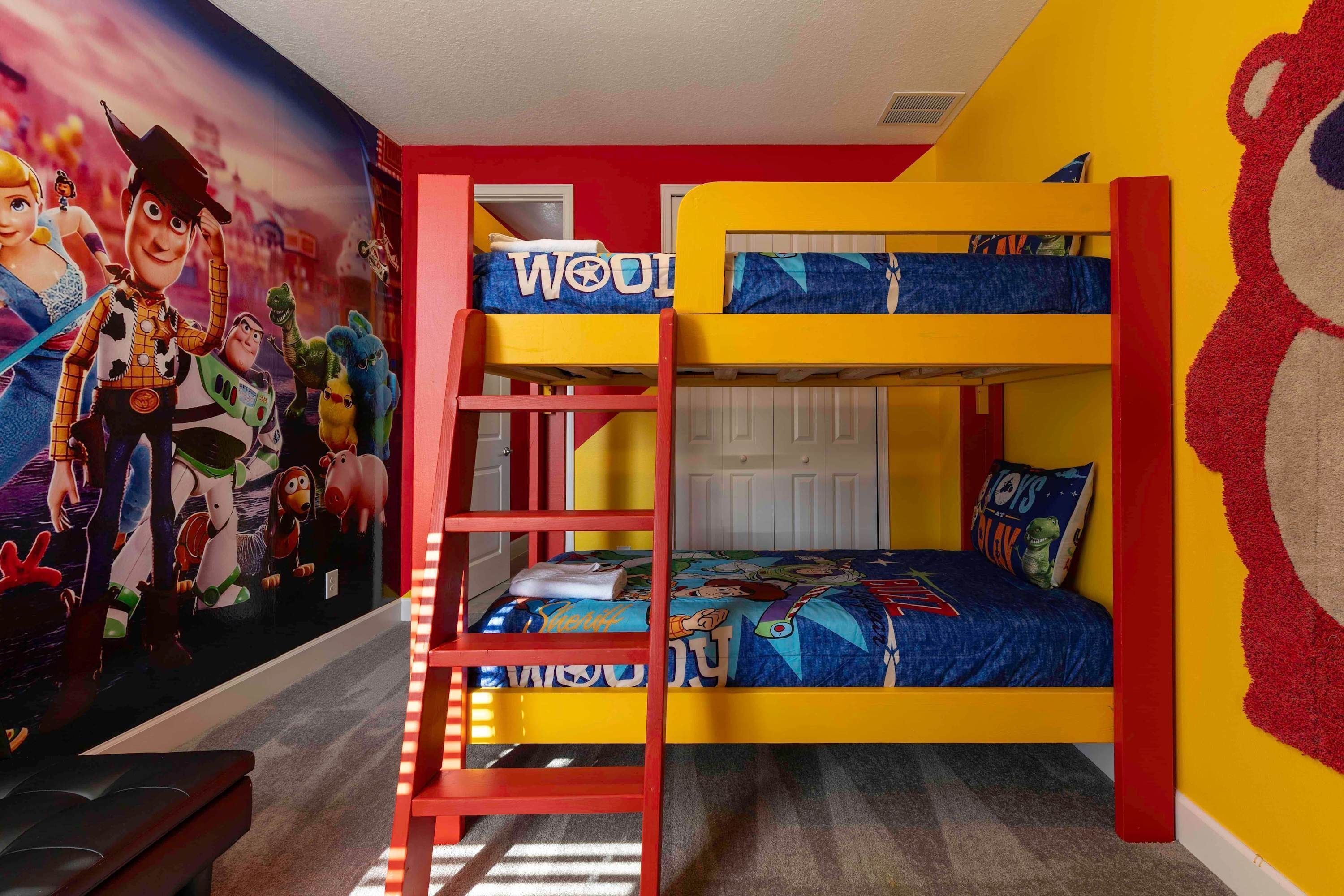 Camera da letto per bambini con letti a castello, un murale con personaggi animati e una scala rossa.
