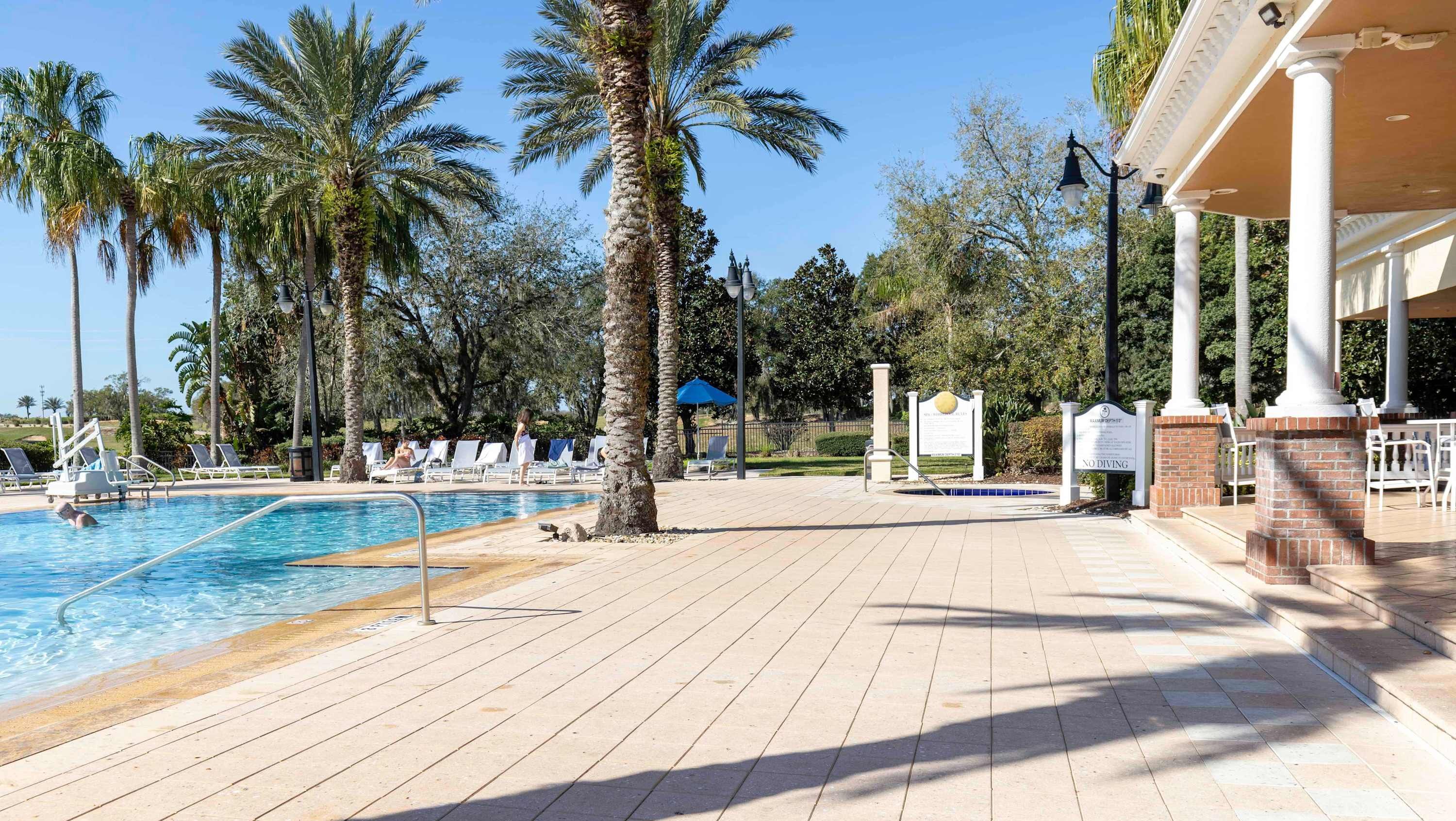 A pool area with lounge chairs, palm trees, and a no diving sign.