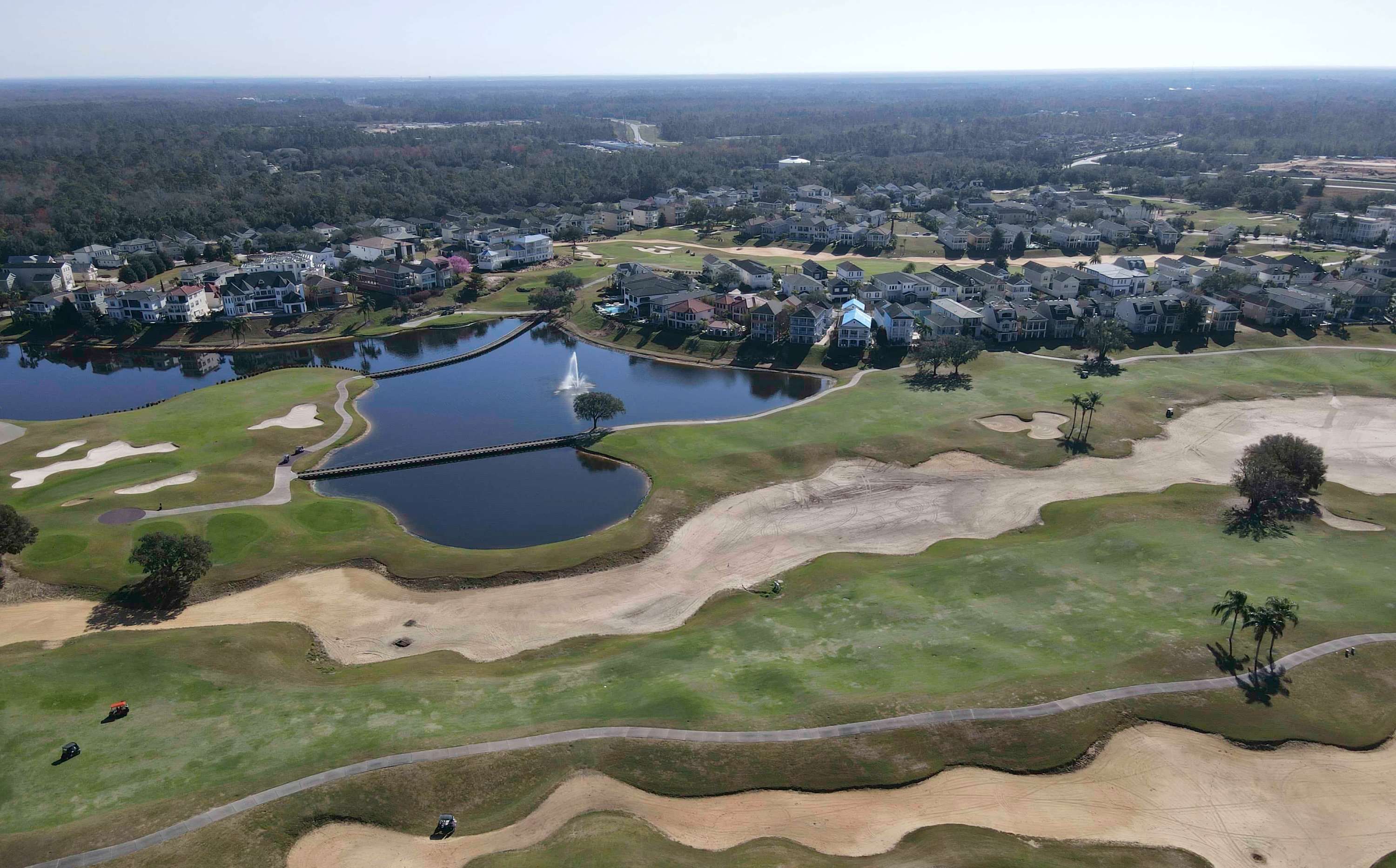 Vue aérienne d’un parcours de golf avec des bunkers de sable, des obstacles d’eau et des zones résidentielles en arrière-plan.