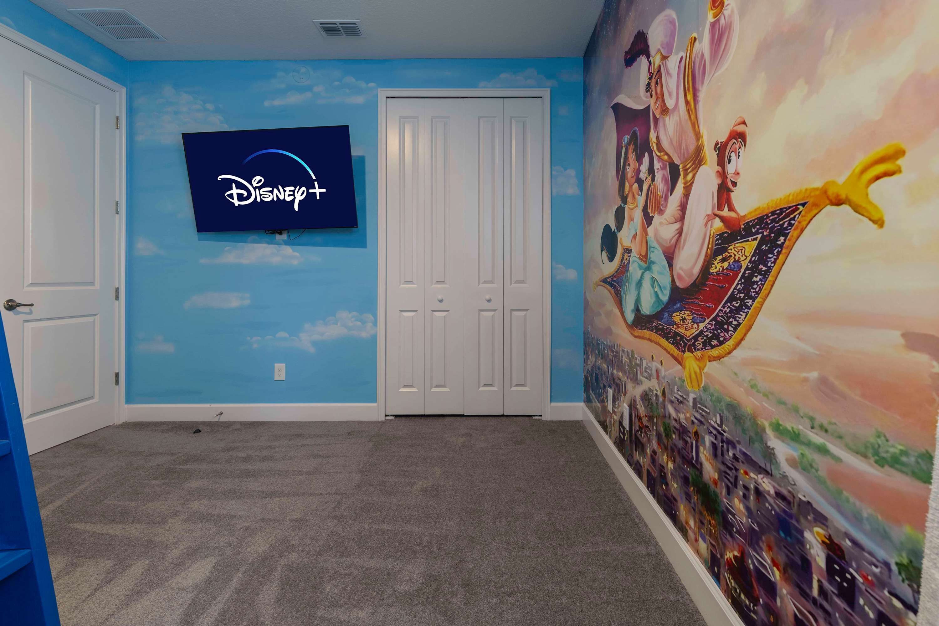 A room with a Disney+ TV mounted on the wall, a white door, and a mural of animated characters.