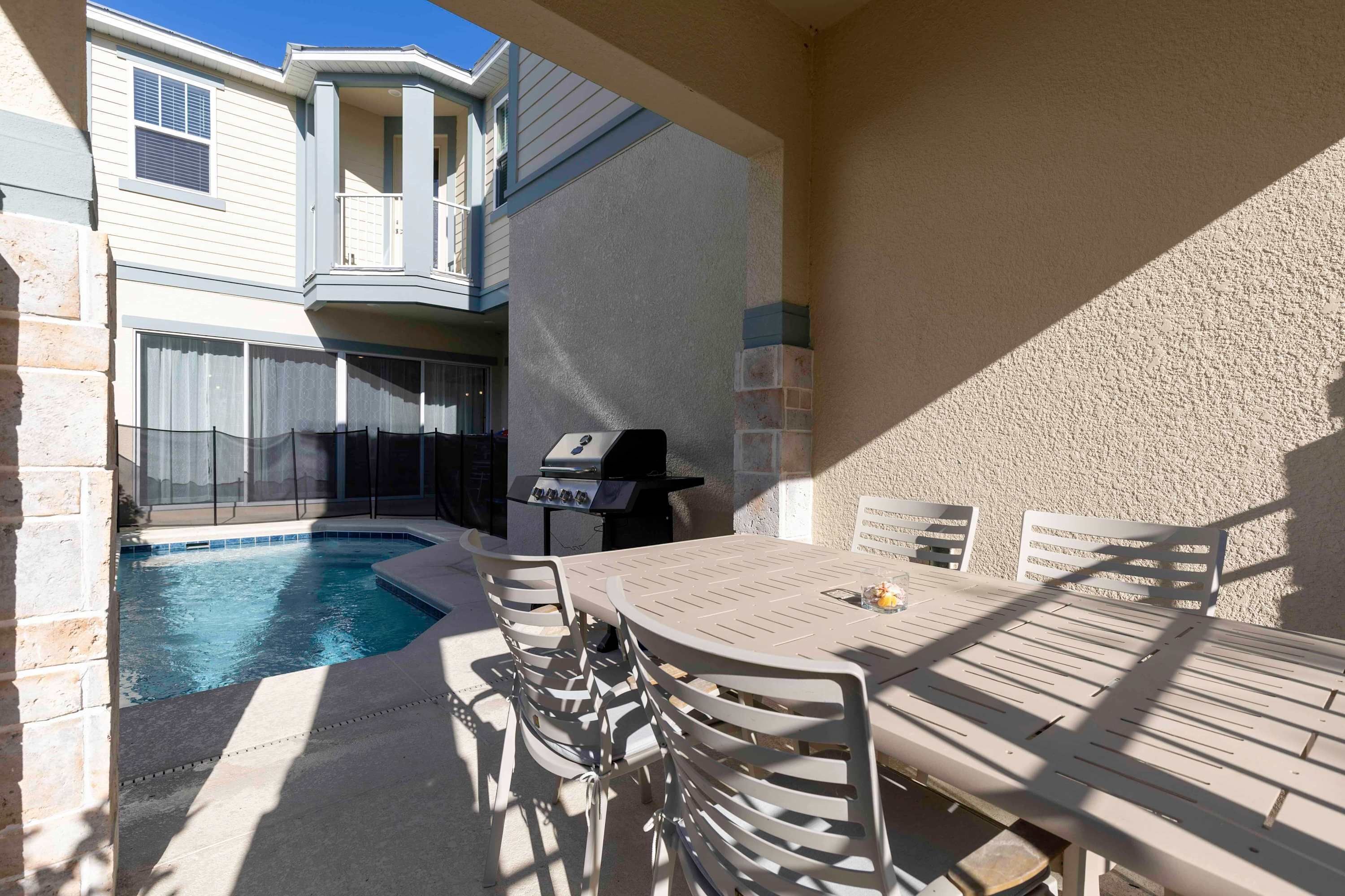 A patio with a pool, outdoor seating, and a grill.