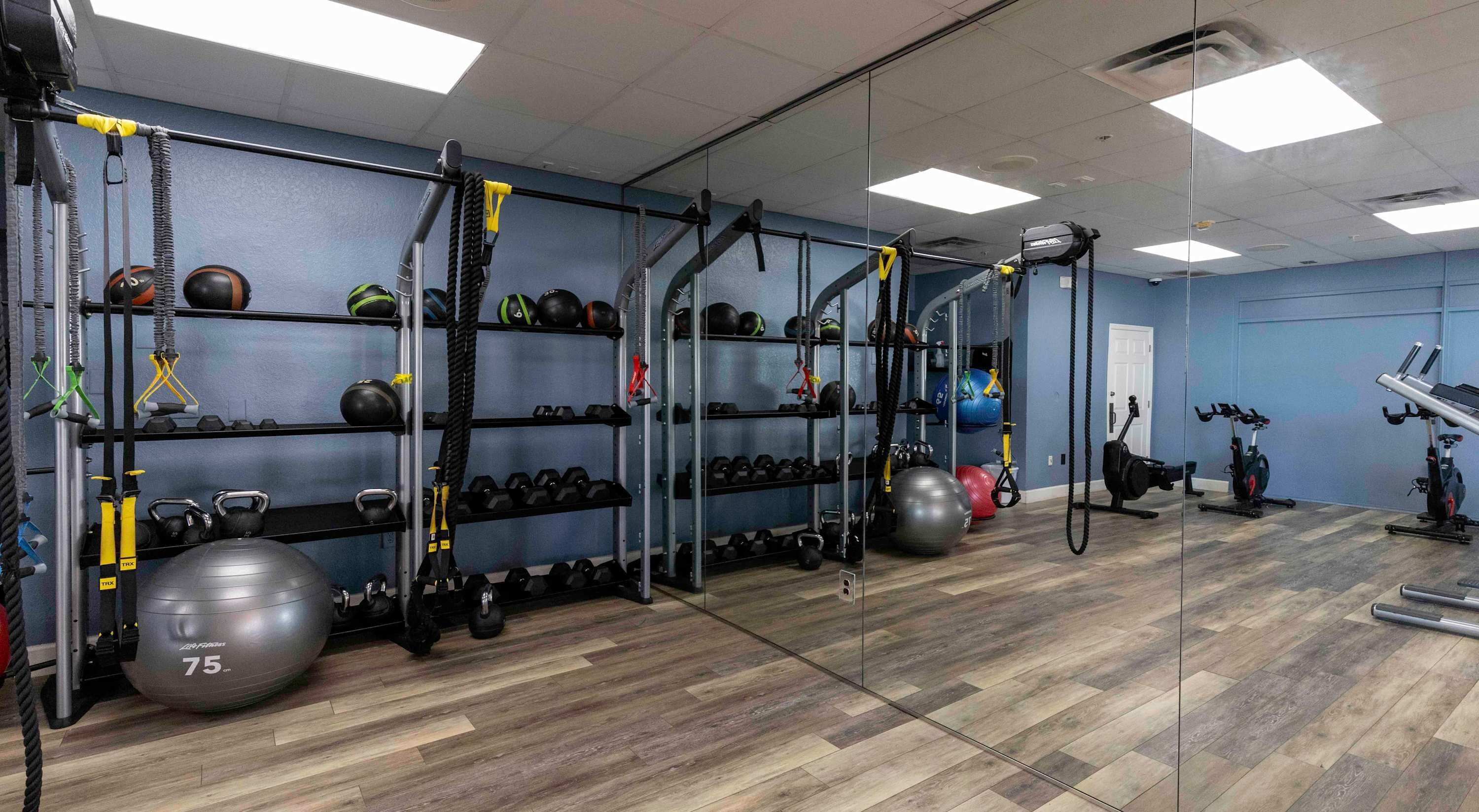 A gym with exercise equipment, weights, and a mirrored wall.