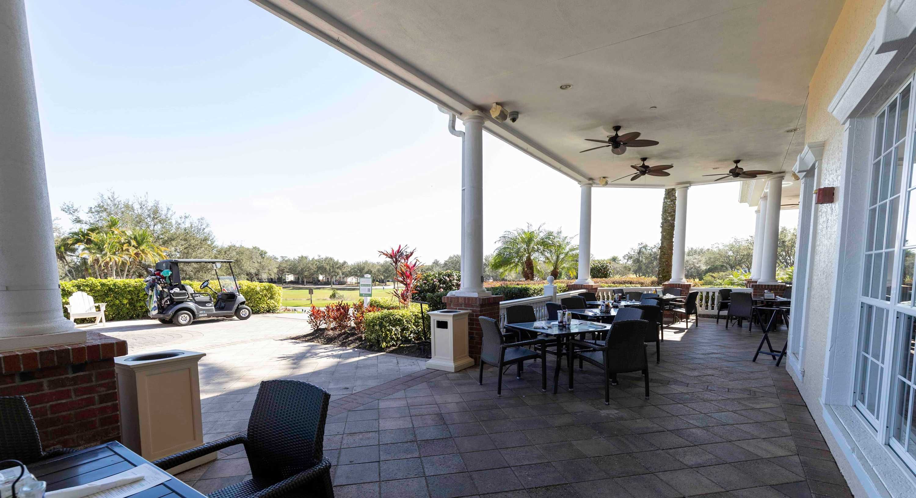 Un patio al aire libre con mesas y sillas, ventiladores de techo y vista a un campo de golf.