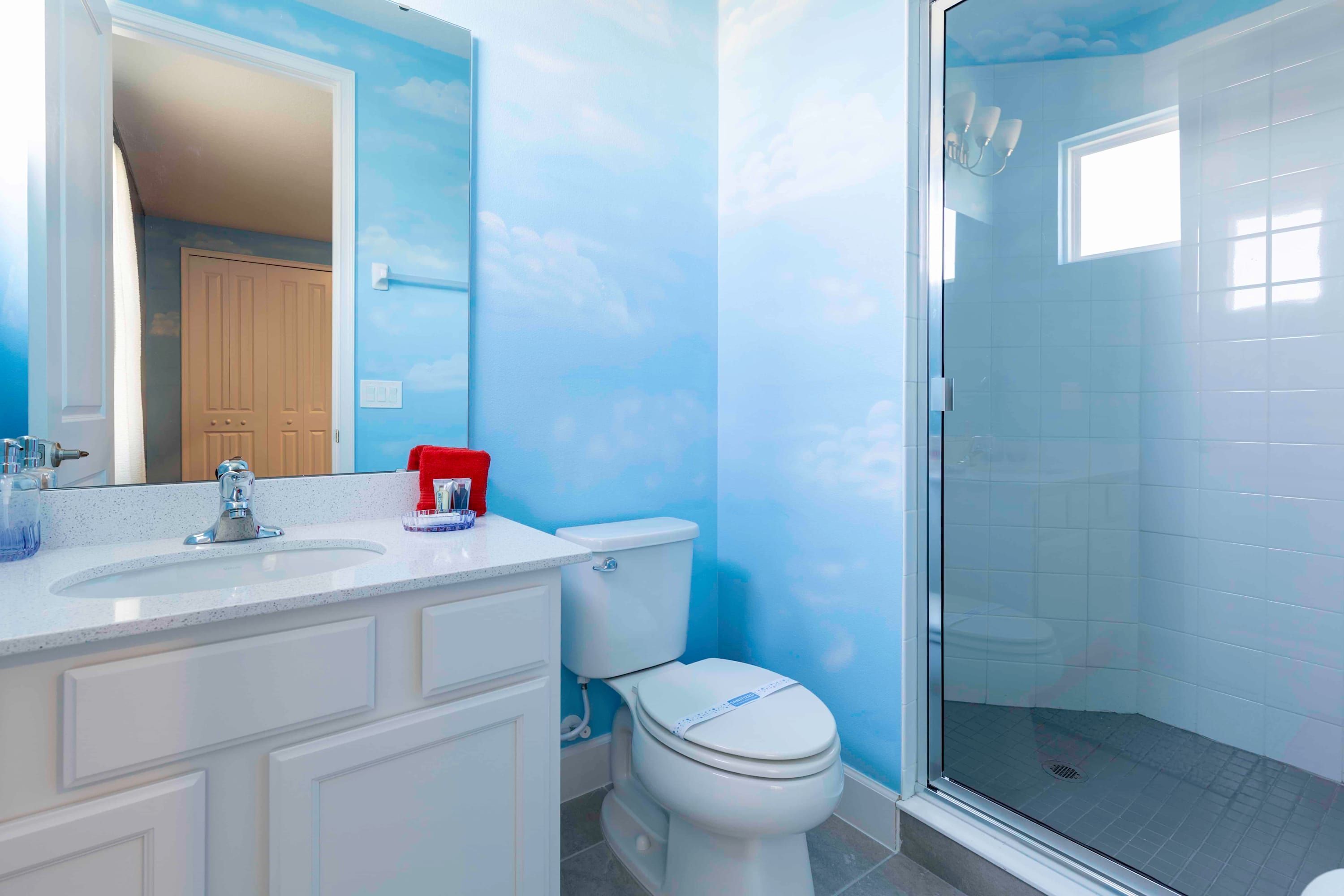 Un bagno con una parete blu, un lavandino bianco, un water e una cabina doccia in vetro.