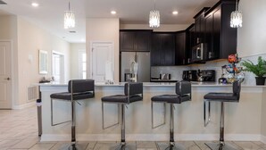 A modern kitchen with dark cabinets, stainless steel appliances, and a central island with bar stools. - Luxury 9BR Villa Poolside Bliss n Pool Table Fun (Kissimmee)