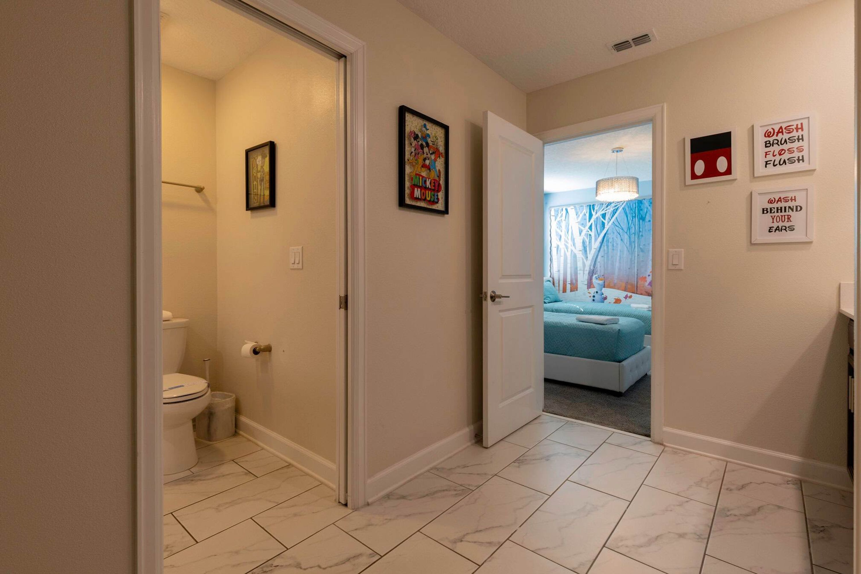 Ein Flur, der zu einem Schlafzimmer mit einem Bett, einem Badezimmer mit einer Toilette und einer Tür zu einem weiteren Raum führt.
