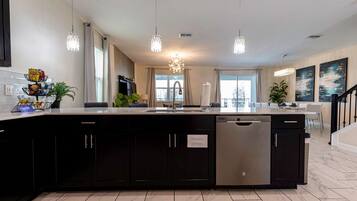 A modern kitchen with a central island, black cabinetry, stainless steel dishwasher, and pendant lighting.