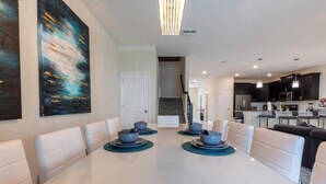 A modern dining area with a white table, blue plates, and white chairs. There is a staircase leading to another level. - Luxury 9BR Villa Poolside Bliss n Pool Table Fun (Kissimmee)