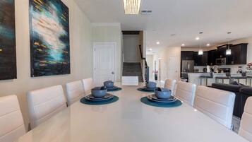 A modern dining area with a white table, blue plates, and white chairs. There is a staircase leading to another level.