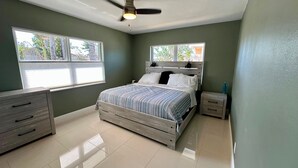 Ein Schlafzimmer mit einem Bett, zwei Nachttischen, einer Kommode und einem Deckenventilator.