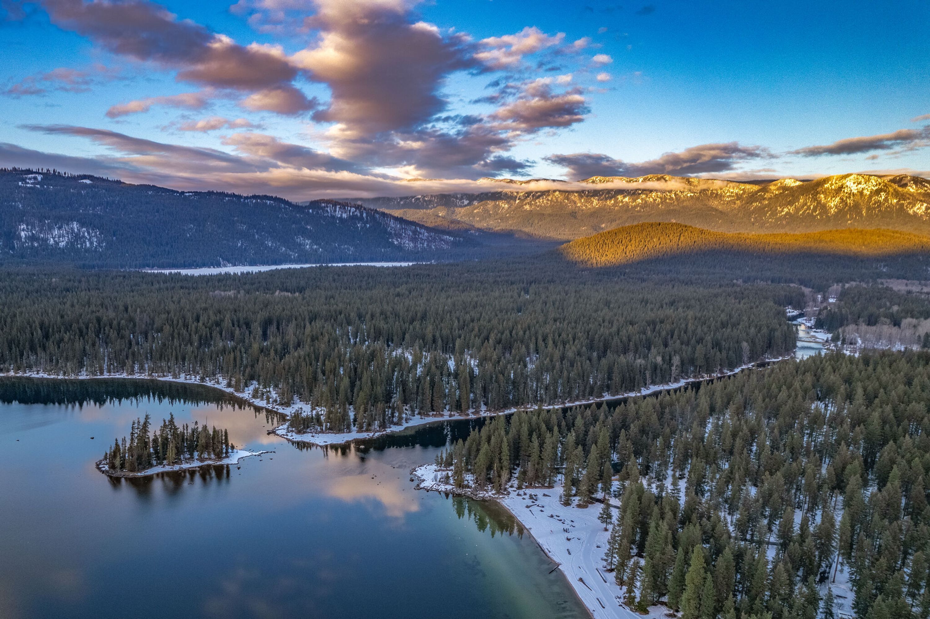 Ein weitreichender Panoramablick auf eine gebirgige Landschaft mit Fluss, dichten Wäldern und schneebedecktem Gelände.