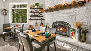 Un coin repas avec une table en bois, des chaises et une cheminée. Des étagères avec des plantes et des objets de décoration sont disposées au-dessus de la cheminée.