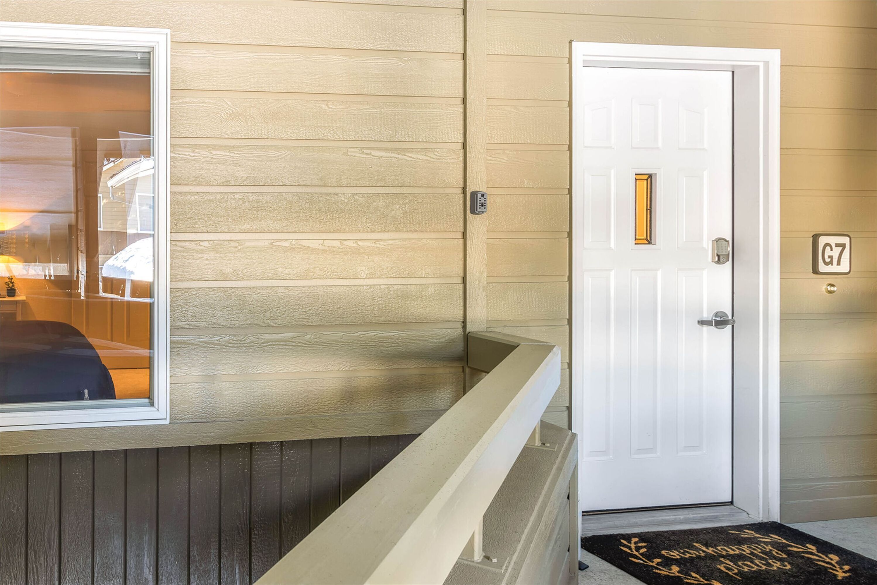 A hotel entrance with a white door marked G7, a small window with a view of the interior, and a doormat with a message.