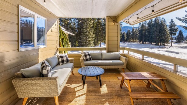 Un espace extérieur abrité, aménagé avec des meubles en osier et une table en bois, offrant une vue sur un paysage enneigé et des arbres.